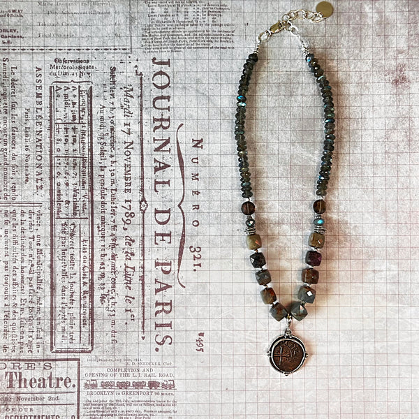 Necklace with beaded chain and an ancient coin pendant on a newspaper