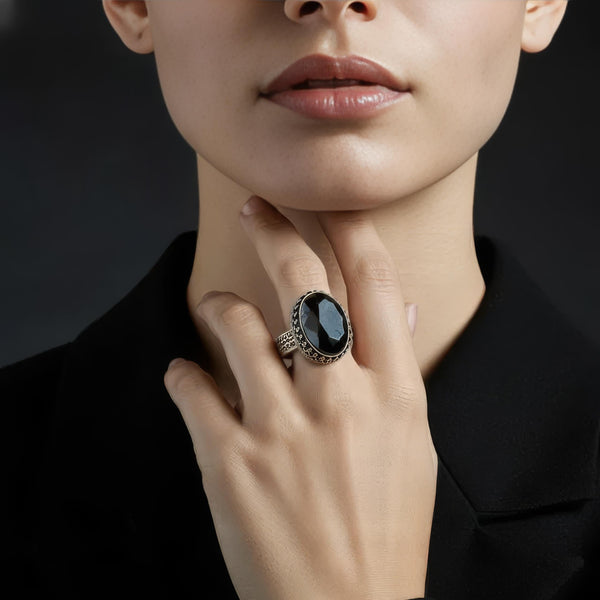 A close-up lifestyle shot of a model wearing a large silver ring with a dark blue oval cabochon stone, set against a dark background.