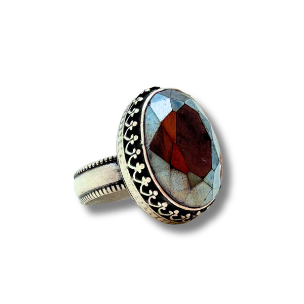 A silver ring featuring a large oval inlay with a faceted gemstone in shades of dark blue, light blue, and gray, set against a plain white background.