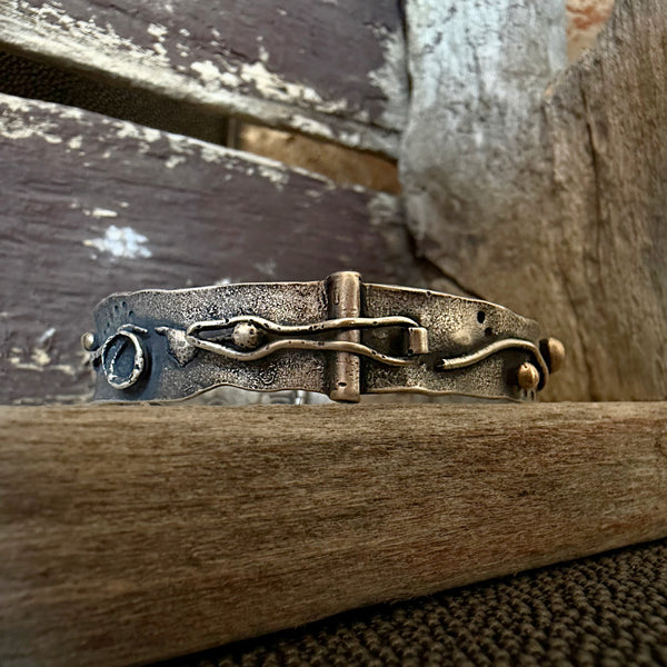 A handmade silver cuff bracelet with a rustic, hammered finish and organic wavy details, resting on a weathered wooden surface.