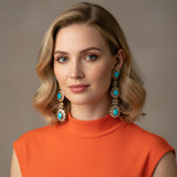 Woman wearing turquoise and diamond slice earrings with an orange top against a neutral background