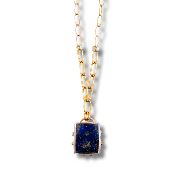 A gold chain necklace featuring the back side of a square lapis lazuli pendant with a silver bezel setting, shown against a plain white background.