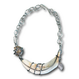The back side of a silver chain necklace featuring a large curved shell pendant wrapped in dark wire, with a small textured shell accent and a small leaf charm, shown on a plain white background.