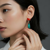 A close-up of a model wearing a drop earring with a rectangular carnelian stone and a teardrop-shaped blue/green stone, set in silver.