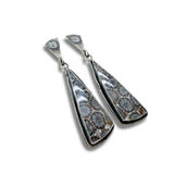 A pair of silver dangle earrings featuring large, teardrop-shaped black fossil coral pendants with a detailed floral or spiderweb-like pattern in gray, white, and brown, set in a twisted rope-style silver border.