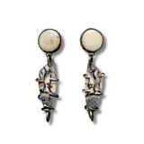 A pair of handmade dangle earrings featuring round cream-colored fossil coral studs at the top and irregular, textured gray and beige fossil wood drops wrapped in dark metal, shown on a plain white background.