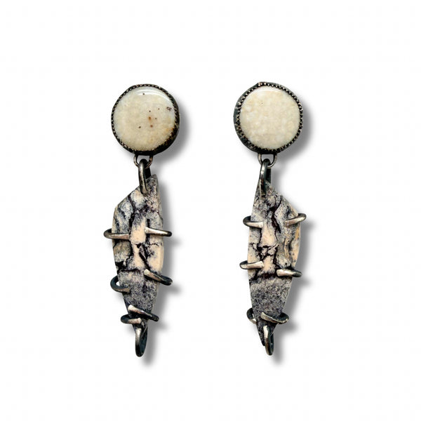 A pair of handmade dangle earrings featuring round cream-colored fossil coral studs at the top and irregular, textured gray and beige fossil wood drops wrapped in dark metal, shown on a plain white background.
