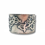 A wide sterling silver cuff ring featuring intricate cutout floral and leaf motifs, displayed on a clean white background with a soft drop shadow.