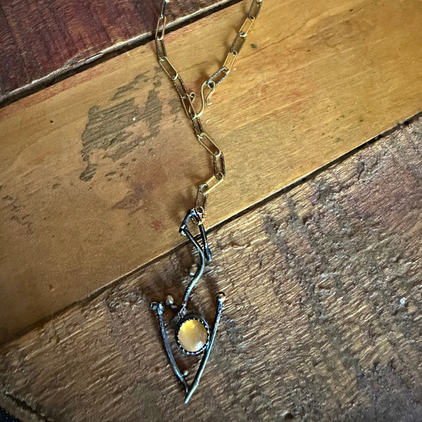 A handmade pendant necklace featuring a gold moonstone cabochon stone surrounded by a silver bezel, set on a rustic wooden background.