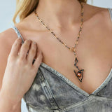 A close-up of a model wearing a gold and black chain necklace with a stylized pendant featuring a small gold moonstone, paired with a gray denim top.