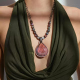 A woman in a dark green dress wears a necklace with a pink labradorite pendant and earth tone square sapphire stones